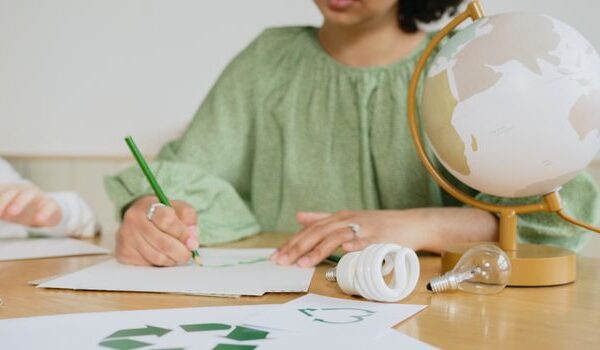 Person drawing recycling symbol at desk with globe and eco-friendly items.